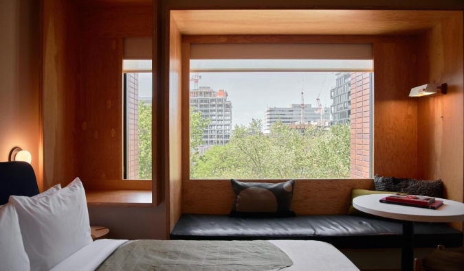 Ένα κρεβάτι μπροστά από ένα παράθυρο εικόνας σε έναν τοίχο με ξύλινη επένδυση, με έναν πάγκο παραθύρου μπροστά του στο ξενοδοχείο Ace στο Τορόντο του Καναδά