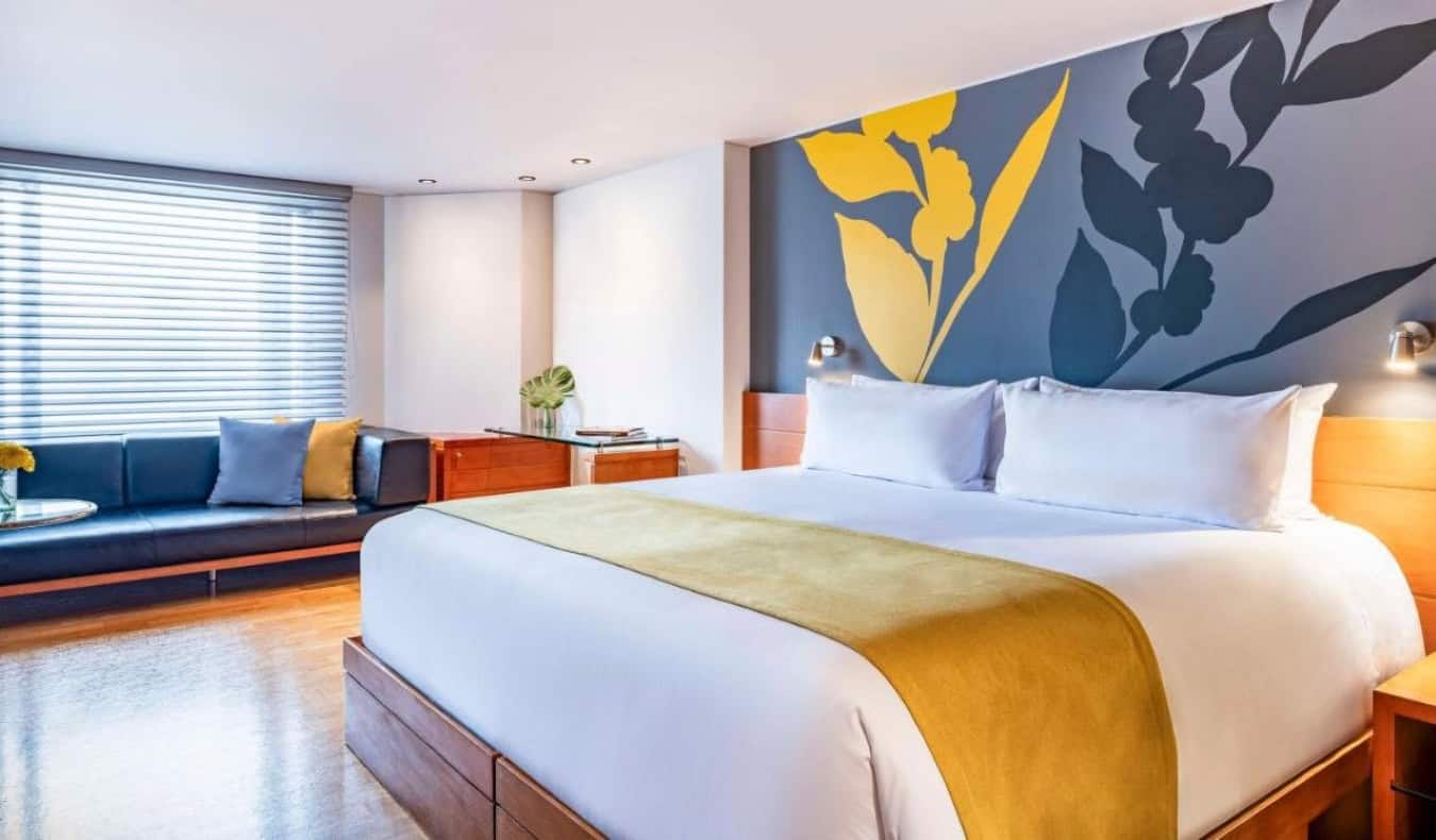 Κρεβάτι king size σε δωμάτιο επισκεπτών με τοίχο βαμμένο με λουλούδια, δάπεδα από μασίφ ξύλο και μεγάλο πάγκο με παράθυρο στο ξενοδοχείο Avani Royal Zona T στη Μπογκοτά, Κολομβία