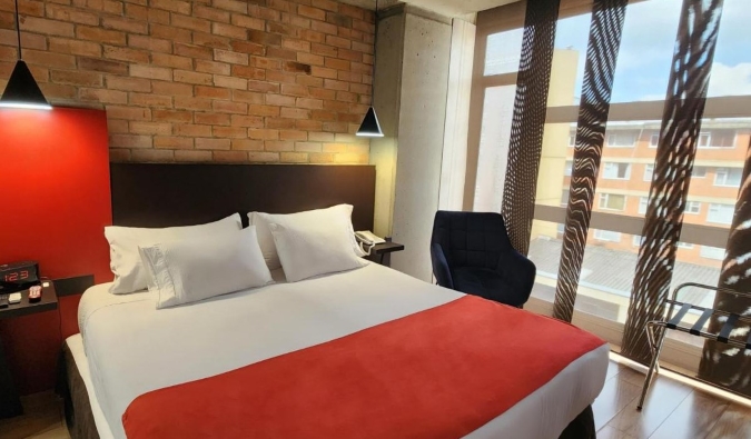 Απλό δωμάτιο με διπλό κρεβάτι μπροστά από έναν εμφανή τοίχο από τούβλα στο Hotel 5 Elementos Apartasuites στη Μπογκοτά, Κολομβία